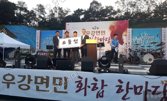 우강면민 화합 한마당 행사에서 관계자들이 소들섬 현판을 들고 기념 촬영을 하고 있다.