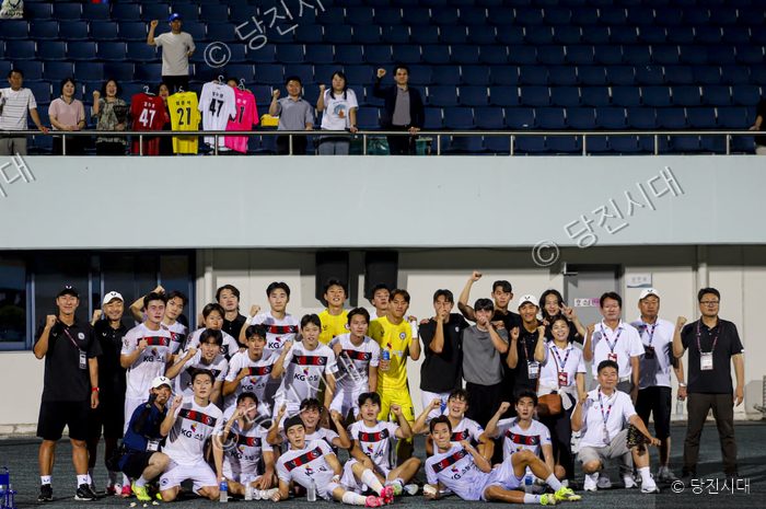 당진시민축구단 선수들과 관계자들이 경기장 관중석을 배경으로 모여 단체 사진을 촬영하고 있다.