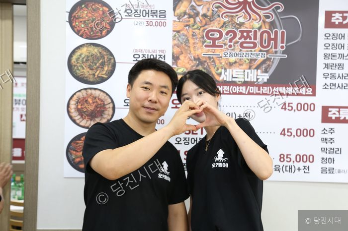 음식점 내부에서 남녀 대표가 손으로 하트를 만들며 포즈를 취하고 있다.