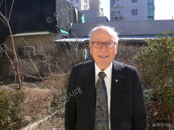 박동원 전 교장이 정원에서 양복을 입고 미소 짓고 있다.