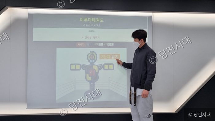 태권도 관장이 스크린의 겨루기 프로그램을 가리키고 있다.