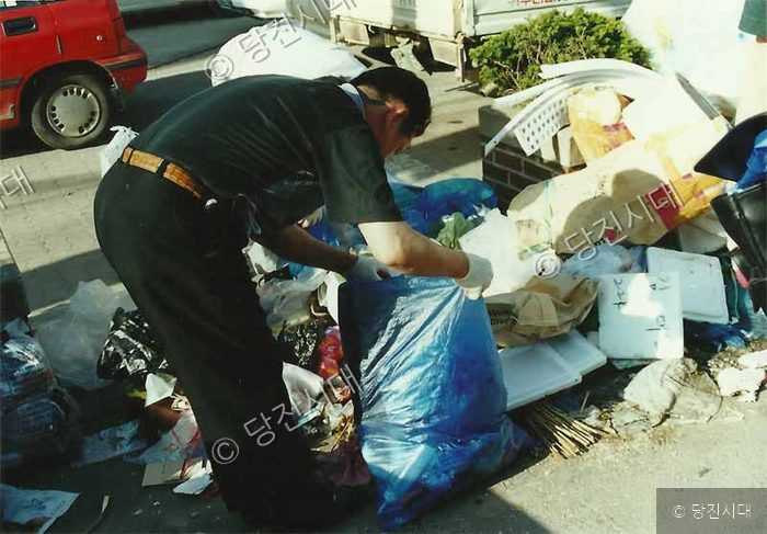 한 남성이 길가에 쌓인 쓰레기를 정리하고 있다.