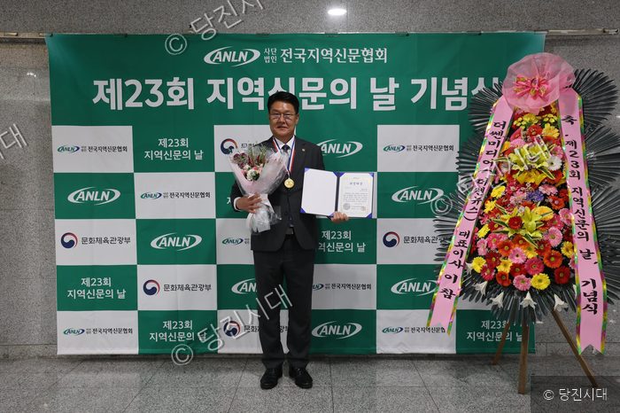 한 남성이 제23회 지역신문의 날 기념식에서 의정대상을 수상하며 상장과 꽃다발을 들고 포즈를 취하고 있다.