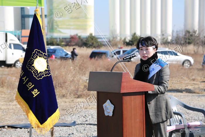 한 여성이 야외에서 발언대 뒤에 서서 마이크를 잡고 말을 하고 있다.