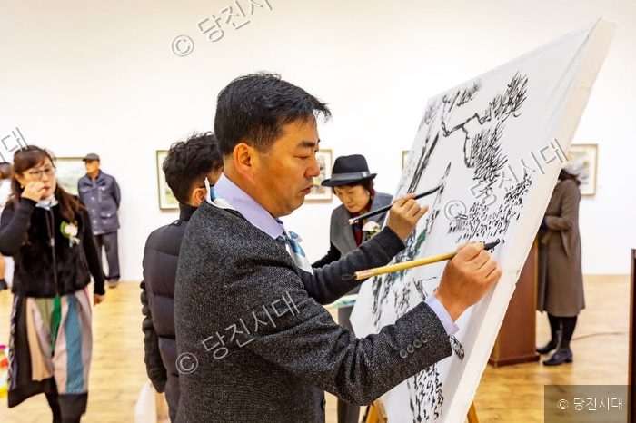 미술관에서 작가들이 대형 캔버스에 수묵화를 그리고 있다.