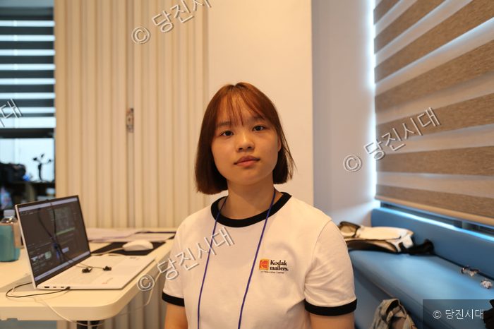청소년이 책상 앞에 앉아 카메라를 바라보고 있다.
