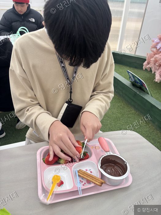 한 아이가 테이블에서 딸기에 초콜릿을 묻히는 체험을 하고 있다.