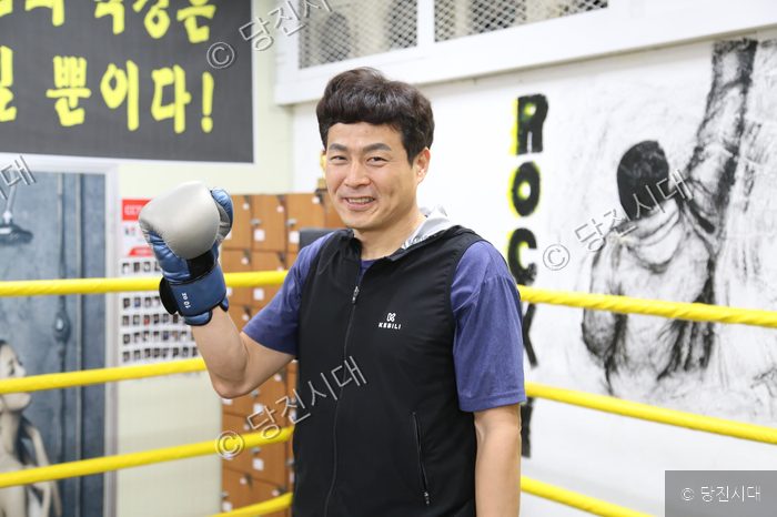 복싱 글러브를 낀 남성이 권투 링 안에서 미소 짓고 있다.