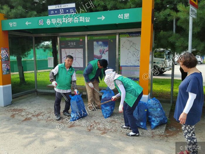 자원봉사자들이 버스정류장 주변에서 쓰레기를 줍고 있다.