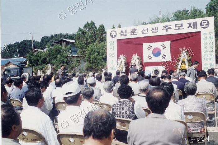 주민들이 야외에서 심훈 선생 추모제 행사에 참석해 앉아 있다.