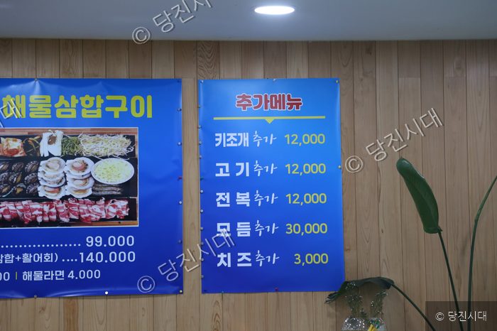 음식점 벽면에 해물삼합구이와 추가 메뉴 가격이 적힌 차림표가 붙어 있다.