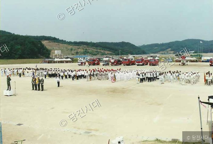 넓은 공터에서 소방차와 사람들이 행사를 진행하고 있다.