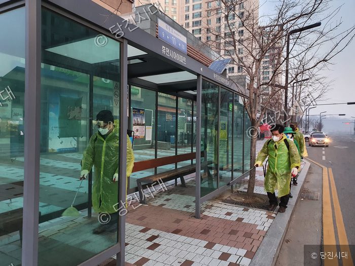 방역복을 입은 자원봉사자들이 버스 정류장에서 방역 활동을 하고 있다.