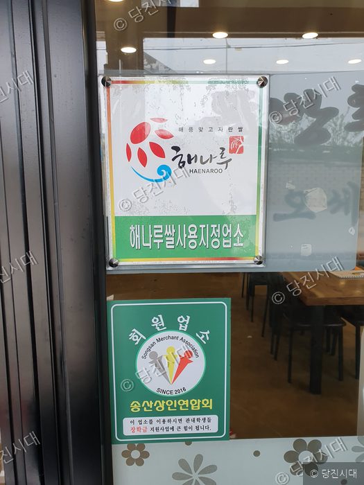 식당 문에 해나루쌀 사용지정업소 인증 표지판과 상인연합회 회원업소 표지판이 부착되어 있다.