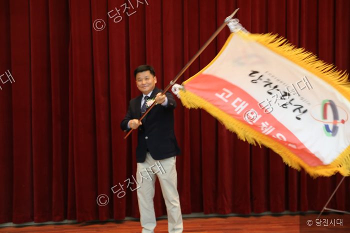 한 남성이 당진시 고대면체육회 깃발을 흔들며 밝게 웃고 있다.