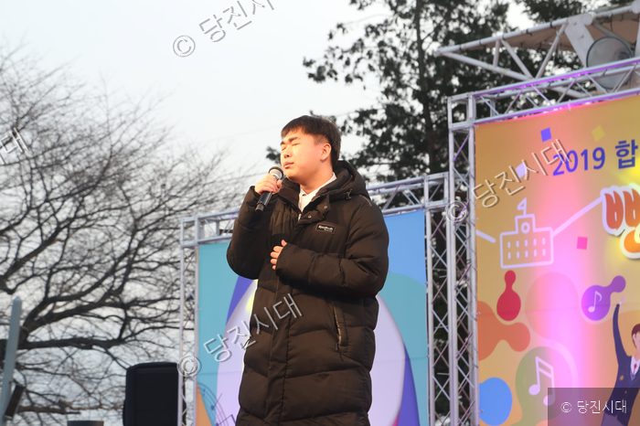한 남성이 야외 무대에서 마이크를 들고 노래를 부르고 있다.