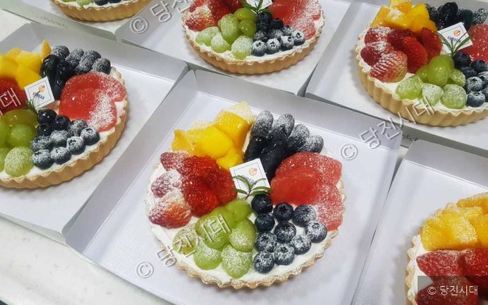 싱싱한 제철 과일이 가득 담긴 맛좋은 타르트가 박스에 담겨 있다.