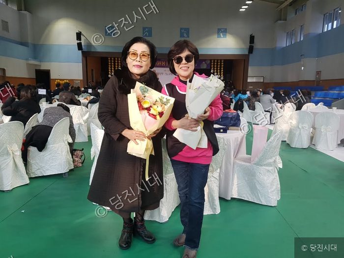 두 여성이 꽃다발을 들고 기념 촬영을 하고 있다.