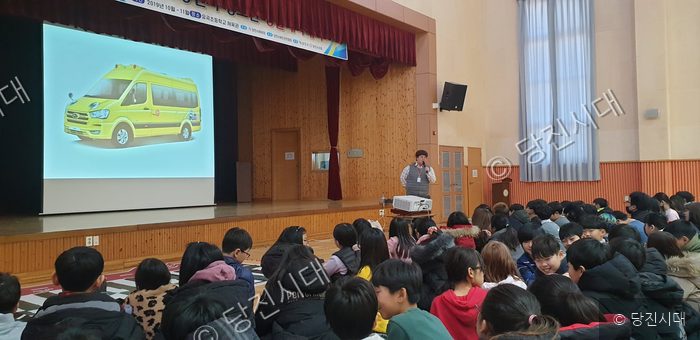 강당에서 학생들이 강사의 교통안전교육 설명을 듣고 있다.