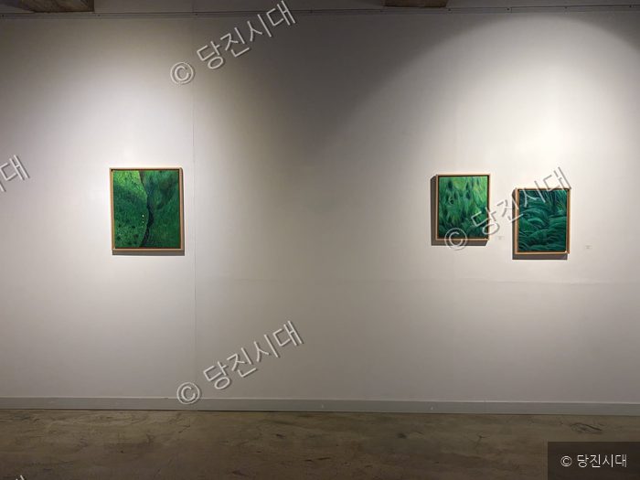 미술관 하얀 벽면에 녹색 계열의 풍경 회화 작품들이 걸려 있다.