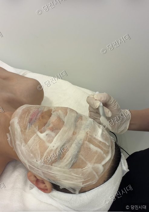 에스테틱 숍에서 원장이 손님에게 피부 팩 관리를 하고 있다.