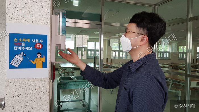 한 남성이 학교 식당 입구에서 손 소독제를 사용하고 있다.