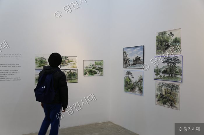 한 관람객이 미술관에서 자연을 주제로 한 그림 작품들을 감상하고 있다.
