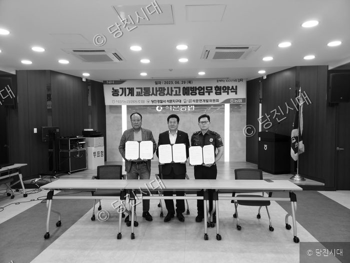 세 사람이 농기계 교통사망사고 예방 업무협약서를 들고 기념 촬영을 하고 있다.