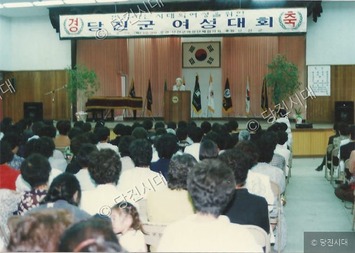 강당에서 당진군 여성대회가 열려 많은 참석자들이 모여 있다.
