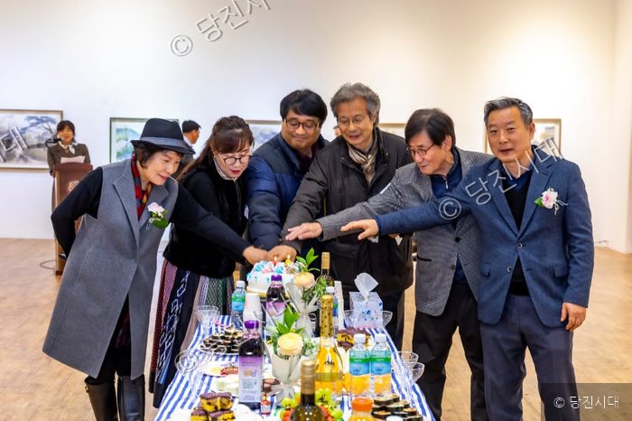 사람들이 케이크 앞에 모여 전시회를 기념하고 있다.