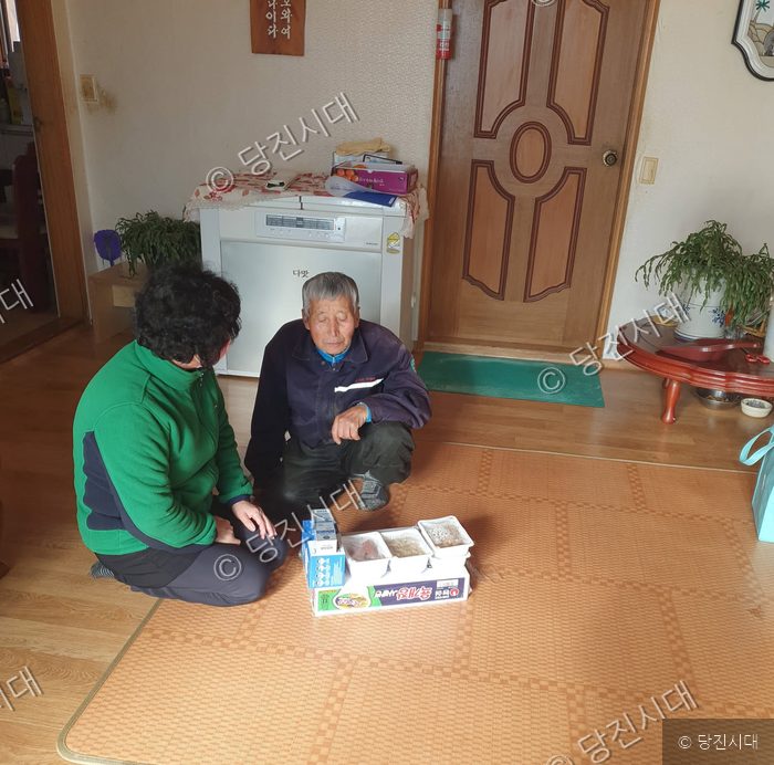 두 어르신이 거실에 앉아 준비된 음식 상을 바라보고 있다.