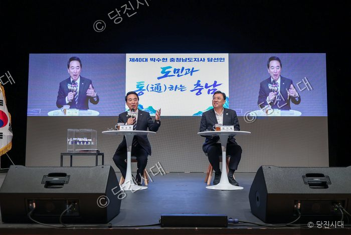 두 남성이 무대 위에서 마이크를 잡고 대화를 나누고 있다.