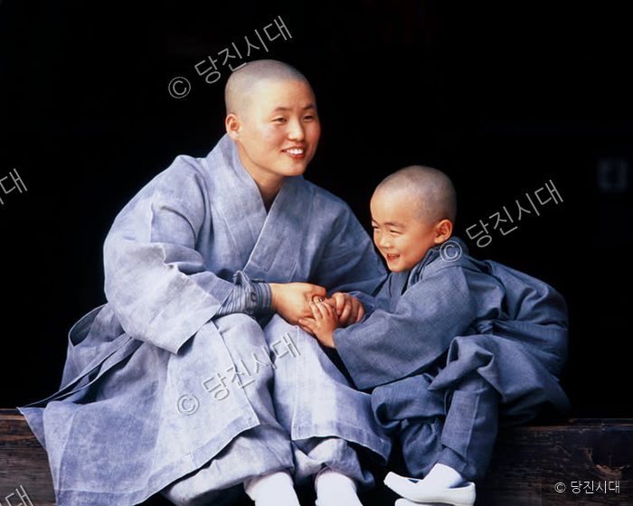 스님과 동자승이 미소를 지으며 손을 잡고 있다.
