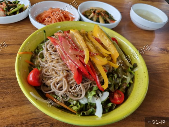 노란 그릇에 담긴 웰빙국수와 여러 가지 밑반찬이 차려져 있다.