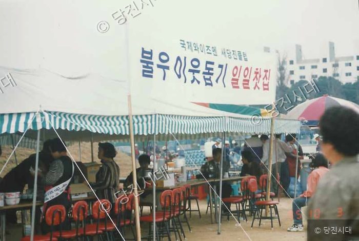천막 아래에서 사람들이 불우이웃돕기 일일찻집 행사를 진행하고 있다.