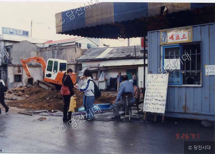 철거 현장 옆 임시 가마와 사람들이 서 있는 풍경.