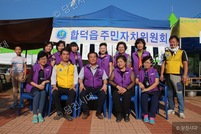 합덕읍 주민자치위원회 관계자들이 야외 부스 앞에서 단체로 기념 촬영을 하고 있다.