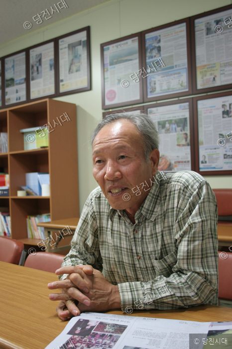 정재석 작가가 책상에 앉아 카메라를 바라보며 미소 짓고 있다.