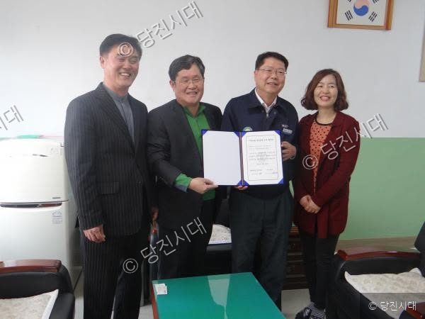 네 명의 남녀가 협약서를 함께 들고 환하게 미소 짓고 있다.