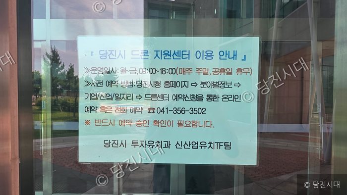 당진시 드론 지원센터의 이용 안내문이 건물 유리문에 부착되어 있다.