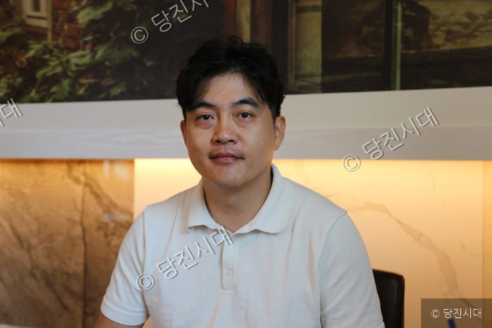 남성이 실내에서 카메라를 바라보며 포즈를 취하고 있다.