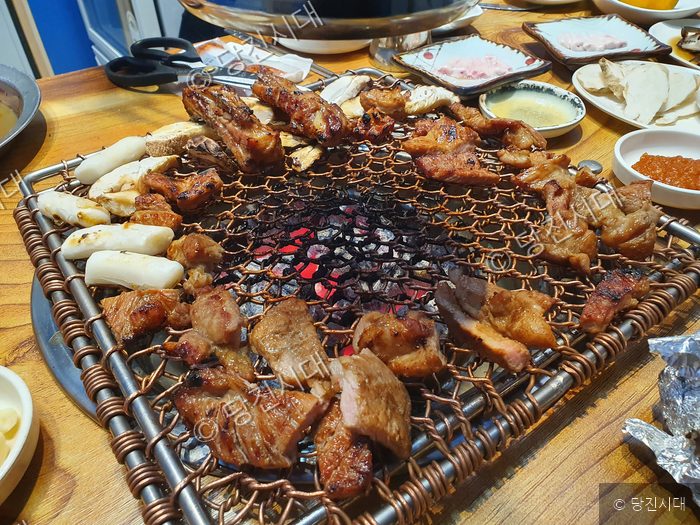 식당 불판 위에 돼지갈비와 고기가 구워지고 있다.