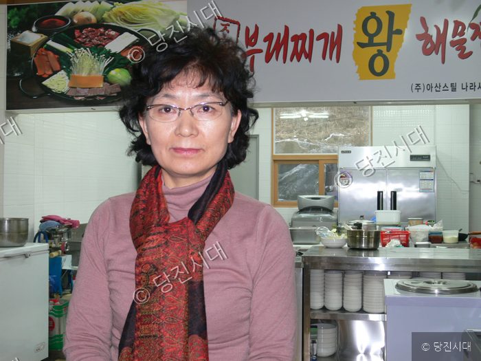 식당 내부에서 주인이 밝은 표정으로 서 있다.