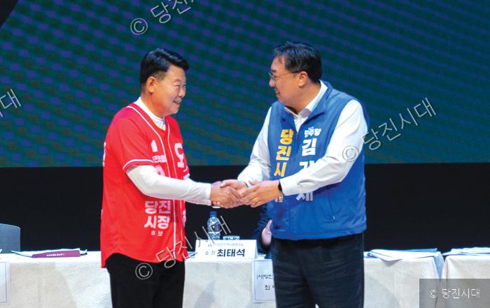 두 남성이 무대 위에서 악수를 나누며 미소 짓고 있다.