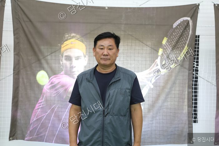 김응규 당진시테니스협회장이 테니스 코트 배경 앞에서 포즈를 취하고 있다.