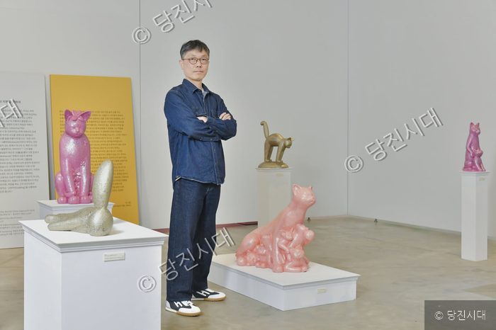 임상준 작가가 고양이 조형물 작품이 전시된 미술관에서 포즈를 취하고 있다.
