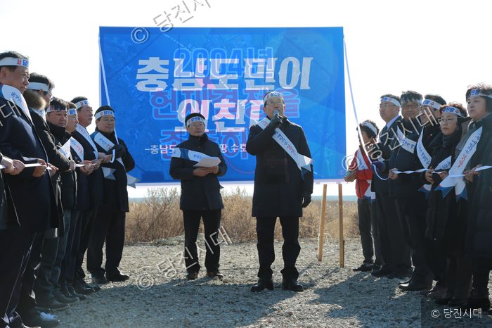 사람들이 야외에서 현수막을 배경으로 행사를 하고 있다.