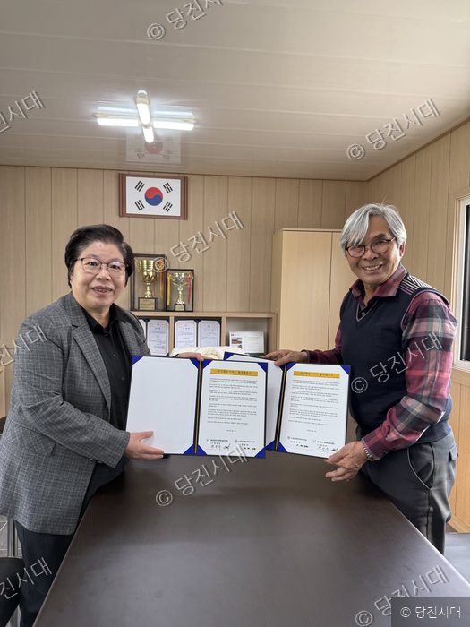 두 남성이 협약서를 들어 보이며 기념 촬영을 하고 있다.