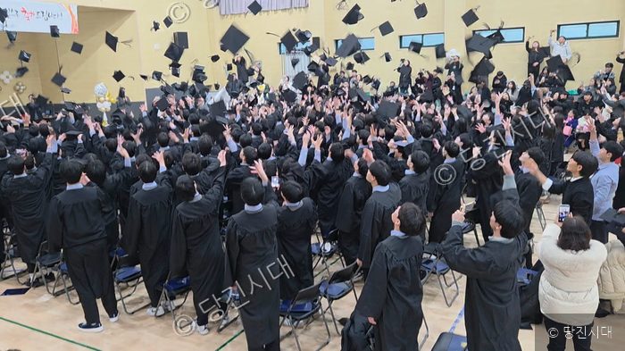 신평고등학교 졸업식에서 학생들이 졸업 가운과 모자를 던지며 환호하고 있다.