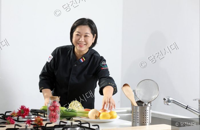 여성이 요리 연구실에서 식재료를 손질하며 미소 짓고 있다.